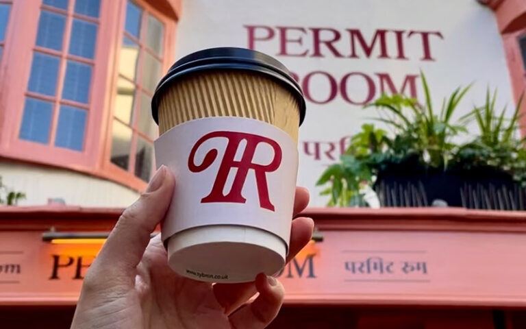 hand holding takeaway cup in front of permit room brighton