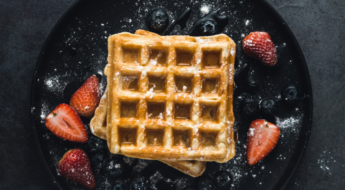 Waffle with sugar and strawberries on a black plate