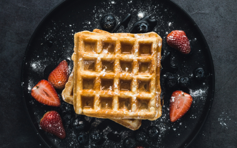 Waffle with sugar and strawberries on a black plate
