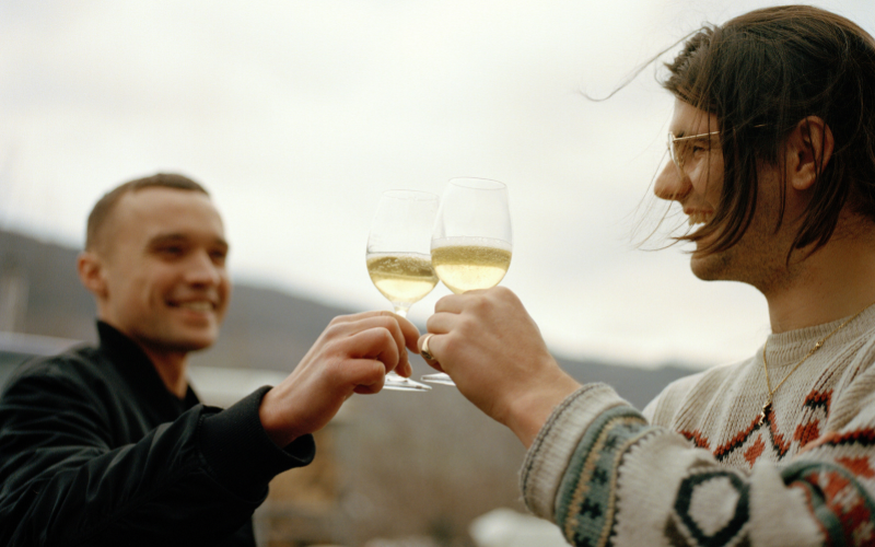 Two men smiling and clinking white wine glasses outside